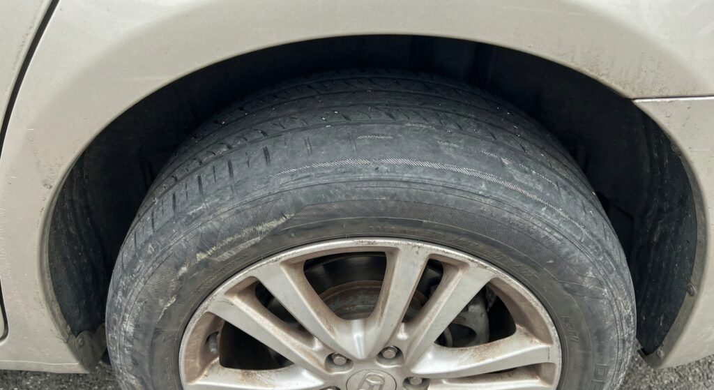 Close-up of a car tire with severe uneven tread wear, showing the inner edge completely bald due to lack of rotation or alignment issues, while the outer edge still has tread.
